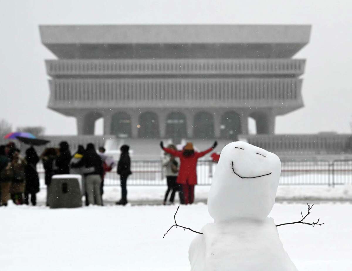 A snowman beams a happy smile from Empire State Plaza as a group of visitors stop for photos on Tuesday, March 14, 2023, in Albany N.Y.