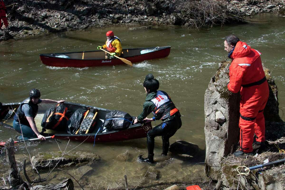 A participant canoes past a couple of participants who fell out of their canoe as they compete in the 48th Annual Tenandeho White-Water Derby on the Anthony Kill on Sunday April 2, 2023 in Mechanicville, N.Y.