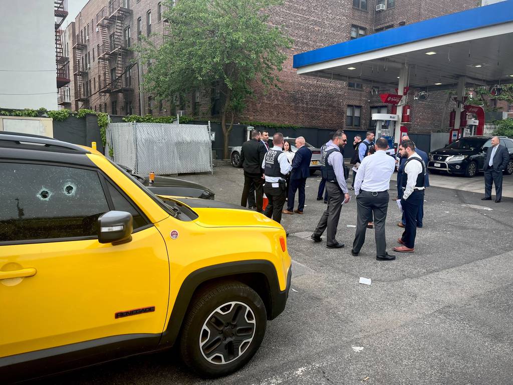 Detectives gather outside a 7-11 on Queens Blvd. A yellow Jeep with bullet holes in the front passenger side window can be seen. 