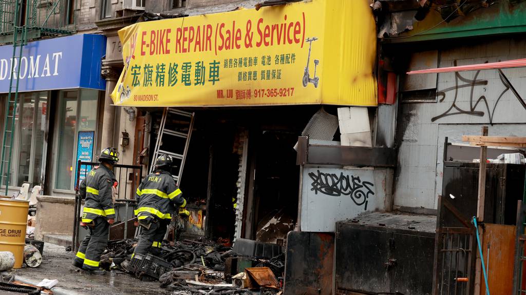 FDNY firefighters check the charred remains of an e-bike repair and sales store on Madison St. in the Chinatown area of Manhattan on Tuesday.