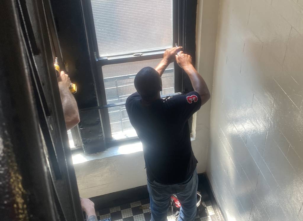 A worker screws a window shut in a common area at the Farragut Road apartment building Tuesday, a day after a 4-year-old boy fell from a fourth-story window to his death.