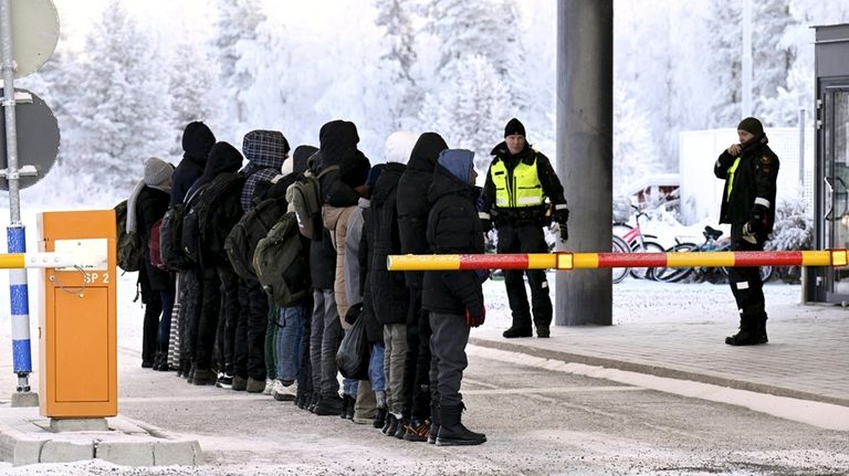 Migrants line up at the international border crossing between Russia...