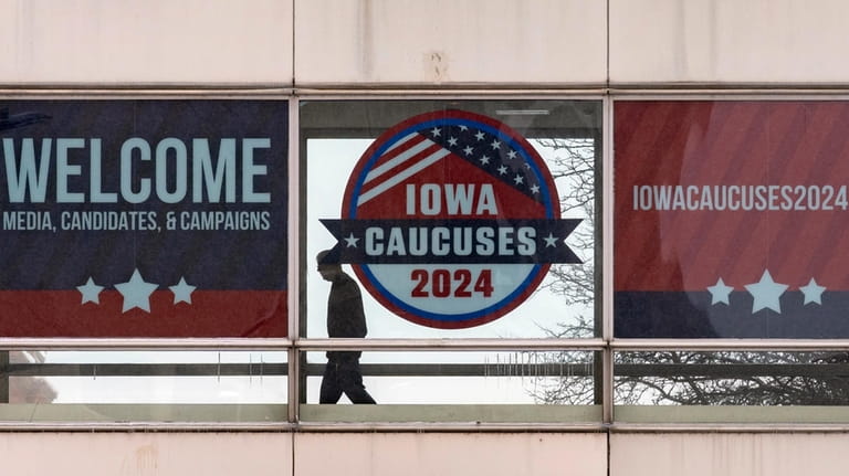 A man walks past a sign that reads "Iowa Caucuses...