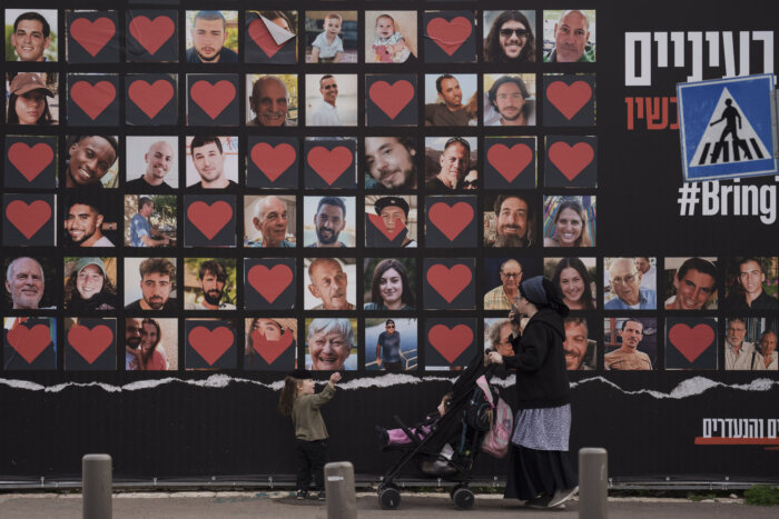 woman walking past photos of hostages in israel